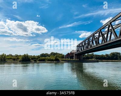 Die Brücke überspannt einen Fluss mit einem blauen Himmel im Hintergrund. Die Brücke besteht aus Metall und ist sehr lang Stockfoto