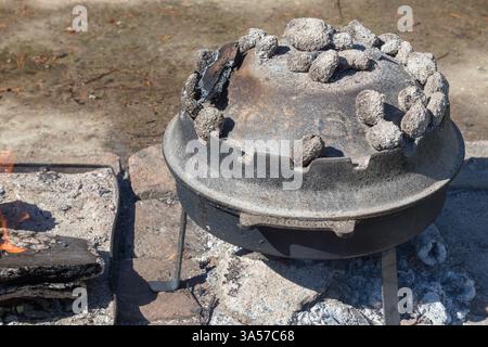 Niederländischer Ofen zum Kochen im Freien auf einem Bett aus heißen Kohlen. Ideal zum Camping, für die Zubereitung herzhafter Mahlzeiten in der Wildnis oder zum Üben traditioneller Kuli Stockfoto