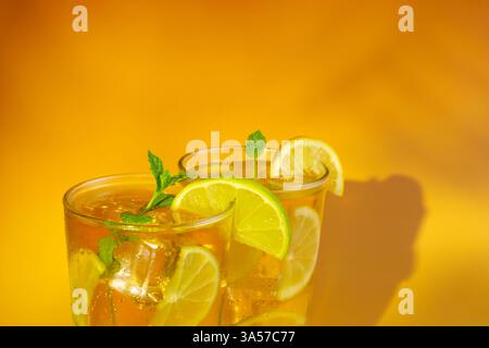 Zwei Gläser Eistee mit Limetten- und Zitronenscheiben darin. Das Getränk wird in einem Glas mit Minzblättern auf der Oberseite serviert. Warmer orangefarbener Hintergrund. Stockfoto