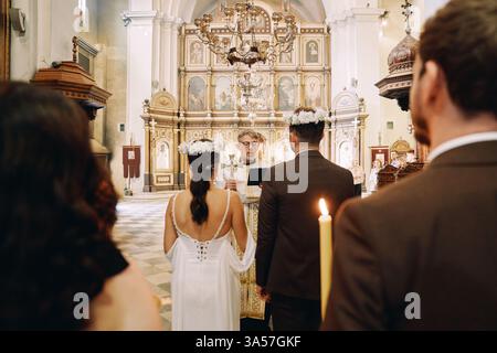 Montenegro, Kotor - 13. Juli 2024: Bester Mann und Brautjungfer stehen mit zündeten Kerzen hinter Braut und Bräutigam bei Zeremonie in der Kirche Stockfoto