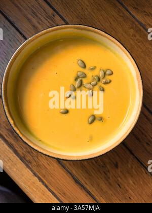 Cremige Kürbissuppe in einer Schüssel serviert, garniert mit Kürbiskernen darauf. Die Suppe wird auf einen Holztisch gestellt. Mit einem Smartphone aufgenommen. Stockfoto