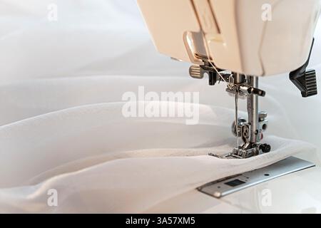 Eine Nähmaschine, die leichte Stoffe zusammennäht und den komplizierten Prozess des Textildesigns und die Schönheit des Nähens unterstreicht. Kopierbereich. Stockfoto