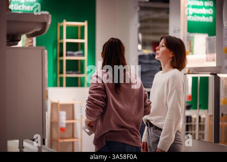 Zwei Frauen durchstöbern einen Laden und inspizieren einen Waschbecken-Schrank im Badezimmer. Der eine greift zu den Details, während der andere beobachtet. Stockfoto