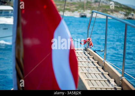 Eine lebhafte türkische Flagge, die stolz auf einer touristischen Yacht winkt und maritimes Abenteuer und Nationalstolz vor dem Hintergrund des offenen Meeres symbolisiert. Stockfoto