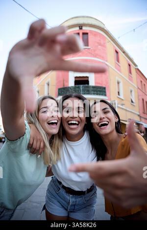 Drei glückliche Freundinnen, die Selfie mit Händen in einer Stadtstraße machen Stockfoto