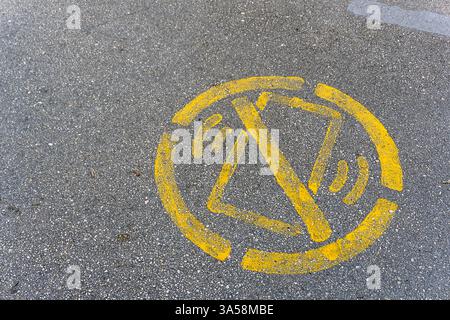 Ein gelbes Symbol auf Asphalt weist darauf hin, dass die Verwendung von Mobiltelefonen während der Fahrt in einer Stadt eingeschränkt ist. Die Warnung ist zur Förderung von Straßen angebracht Stockfoto