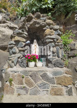 Trevignano Romano, Latium, Italien - 7. Juli 2024: Marienstatue in der Grotte mit einem Topf rosa Blumen vor der Via Guiseppe Garibaldi Süd End Stockfoto