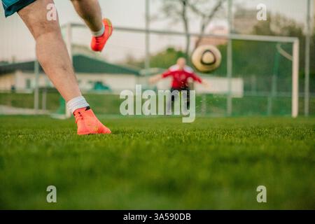 Low-Angle-Ansicht der Fußballer-Beine, während der Ball in Richtung Torwart geschleudert wird Stockfoto
