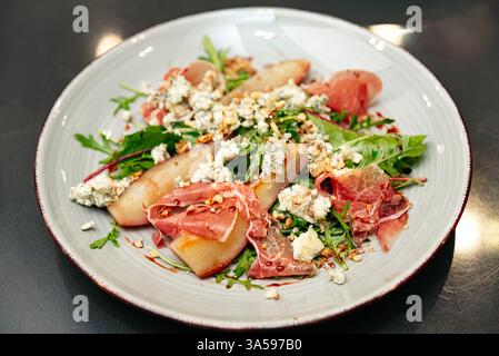 Ein Gourmet-Salat mit pochierten Birnen, Schinken, Blauschimmelkäse, gemischtem Gemüse und kandierten Nüssen, mit Balsamico-Glasur auf einem Teller getränkt. Stockfoto