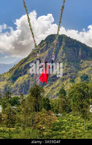 Eine Frau schwingt hoch über den üppigen Hügeln von Ella, Sri Lanka, mit Little Adam's Peak im Hintergrund und genießt ein aufregendes und landschaftlich reizvolles Abenteuer in n Stockfoto
