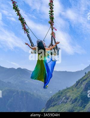 Eine Frau schwingt hoch über den üppigen Hügeln von Ella, Sri Lanka, mit Little Adam's Peak im Hintergrund und genießt ein aufregendes und landschaftlich reizvolles Abenteuer in n Stockfoto