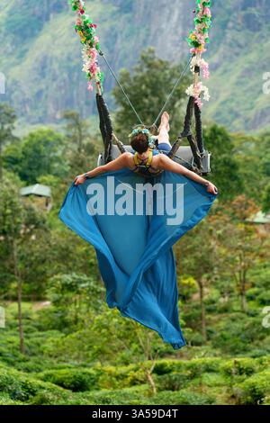 Eine Frau schwingt hoch über den üppigen Hügeln von Ella, Sri Lanka, mit Little Adam's Peak im Hintergrund und genießt ein aufregendes und landschaftlich reizvolles Abenteuer in n Stockfoto