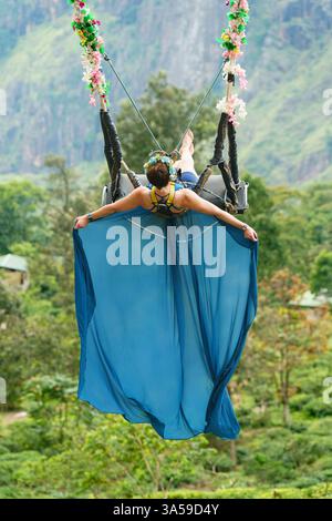 Eine Frau schwingt hoch über den üppigen Hügeln von Ella, Sri Lanka, mit Little Adam's Peak im Hintergrund und genießt ein aufregendes und landschaftlich reizvolles Abenteuer in n Stockfoto