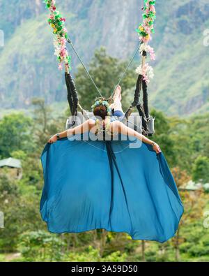Eine Frau schwingt hoch über den üppigen Hügeln von Ella, Sri Lanka, mit Little Adam's Peak im Hintergrund und genießt ein aufregendes und landschaftlich reizvolles Abenteuer in n Stockfoto