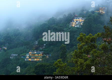 Das Bild fängt die nebeligen Täler von Ella, Sri Lanka, mit üppigen grünen Bergen ein, die teilweise von Wolken bedeckt sind. Am Rande steht ein Gebäude am Hang Stockfoto