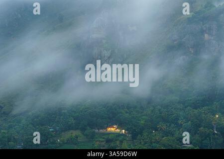 Das Bild fängt die nebeligen Täler von Ella, Sri Lanka, mit üppigen grünen Bergen ein, die teilweise von Wolken bedeckt sind. Am Rande steht ein Gebäude am Hang Stockfoto