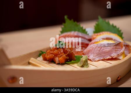 Sashimi-Set mit Lachs, serviert auf einem hölzernen Sushi-Boot, mit Zitrone und Wasabi Stockfoto