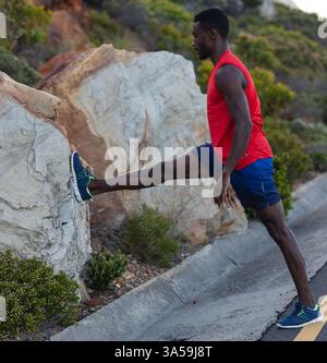 Sportlicher Mann, der das Bein auf dem Felsen beim Workout im Freien in der Natur streckt Stockfoto