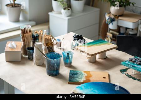 Epoxidkunststoffe für Wasserwellenmuster. Tisch überfüllt mit Pinselfarben und Platten mit trocknenden Kunstwerken Stockfoto