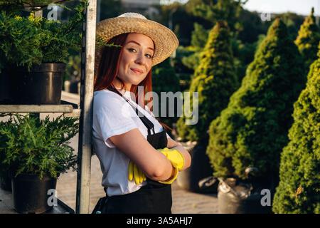 Im Strohhut. Die junge rothaarige Frau kümmert sich um den Garten. Stockfoto