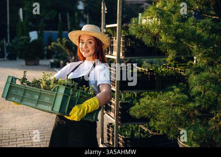 Unter der Sonne, Pflanzen halten. Die junge rothaarige Frau kümmert sich um den Garten. Stockfoto