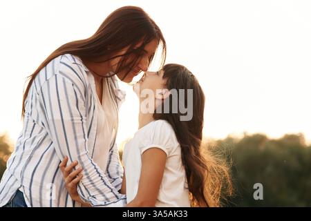 Blick von der Seite, Blick auf einander. Mutter mit ihrer liebenswerten Tochter ist draußen auf dem Feld. Stockfoto