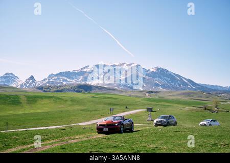 Montenegro, Zabljak - 09. Mai 2024: Autos fahren auf einer Landstraße entlang einer Autobahn in einem Tal vor dem Hintergrund verschneite Berge Stockfoto