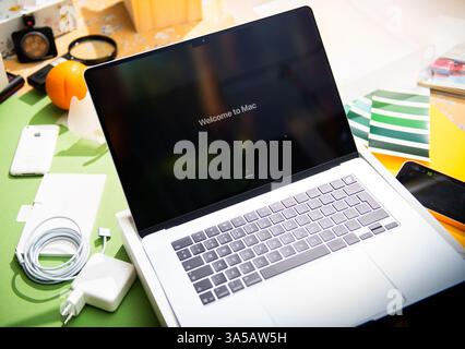 Paris, Frankreich – 13. März 2025: Das MacBook Air M4 zeigt während der Ersteinrichtung Willkommen beim Mac an, umgeben von Ladegerät, Kabel, Telefonen und Farbbeispiel Stockfoto