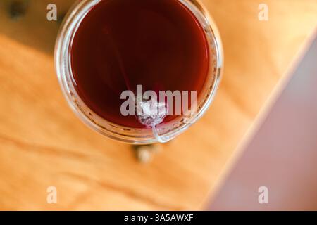 Roter Tee oder auch „Drachenblut Tee“ genannt im kleinen Klarglas auf Holztisch Stockfoto