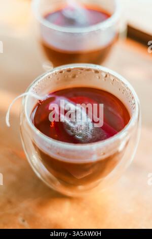 Roter Tee oder auch „Drachenblut Tee“ genannt im kleinen Klarglas auf Holztisch Stockfoto