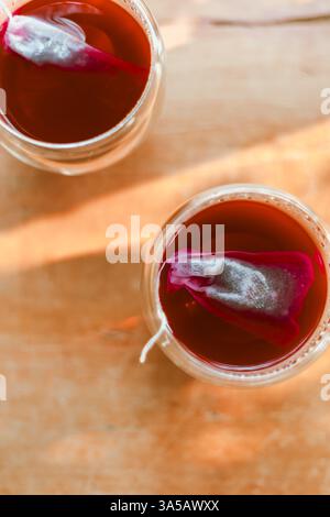 Roter Tee oder auch „Drachenblut Tee“ genannt im kleinen Klarglas auf Holztisch Stockfoto