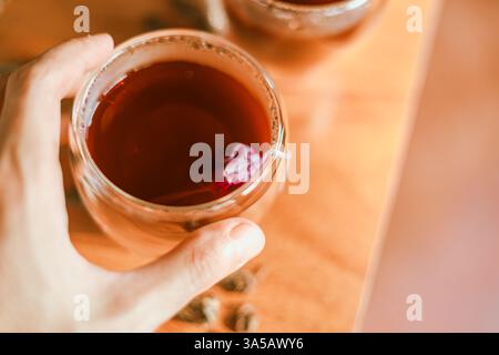 Roter Tee oder auch „Drachenblut Tee“ genannt im kleinen Klarglas auf Holztisch Stockfoto