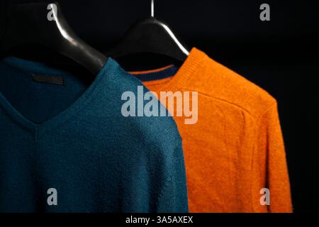 Eine Nahaufnahme, die die weiche Stoffstruktur eines einfarbigen Sweatshirts in Marineblau und Orange auf einem Kleiderbügel vor schwarzem Hintergrund hervorhebt. Pro Stockfoto