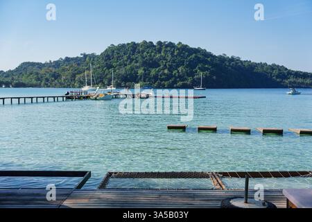 Tropisches Seebad mit Hängematte über dem Wasser, Holzpier und Booten an sonnigen Tagen auf Koh Kood Island Stockfoto