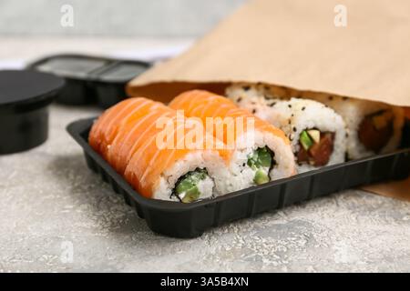 Plastikteller mit leckeren Sushi-Rollen und Papiertüte auf hellem Grunge-Hintergrund, Nahaufnahme. Lieferkonzept Stockfoto