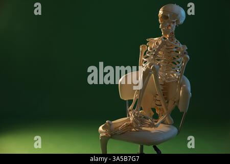 Künstliches menschliches Skelettmodell, das auf Stuhl vor grünem Hintergrund sitzt, Raum für Text Stockfoto