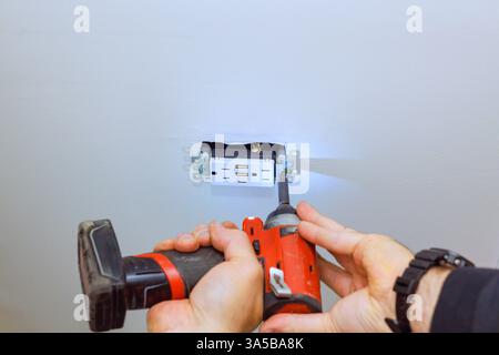 Der Arbeiter verwendet ein Elektrowerkzeug, um eine neue Steckdose an der Decke zu installieren, wobei er sich auf die Sicherheit der Präzision konzentriert. Stockfoto