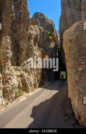 Aufnahme eines Needles Highway, der sich durch einen Tunnel schlängelt, der in hohen Felsformationen geschnitzt ist, wobei ein Motorradfahrer aus dem Tunnel unter einem c hervortritt Stockfoto