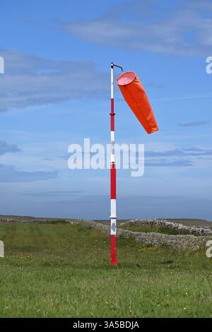 Rote Windsocke an rot-weiß gestreiften Stangen auf dem Flugplatz Papa Westray Orkney Stockfoto