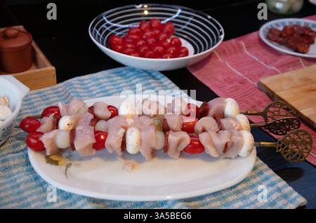 Ein weißer Vintage-Teller mit drei Kebab-Spießen mit Hühnchen, Kirschtomaten, Zwiebeln und Wurst Stockfoto