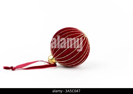 Auf einem weißen Hintergrund liegt an der Seite rotes rundes Samtbaumspielzeug mit goldenen Paspeln an einem roten Seil Stockfoto