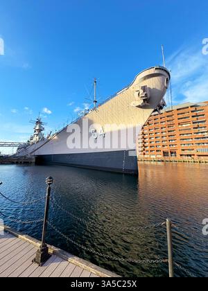Das riesige Kriegsschiff der USS Wisconsin aus der Zeit des Zweiten Weltkriegs legte am 20. November 2023 in Norfolk, Virginia, unter einem klaren blauen Himmel neben Gebäuden am Wasser an. Stockfoto