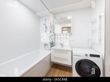 Helles und modernes Bad mit Badewanne, Waschmaschine, Waschbecken mit Stauraum und einer hellen Farbpalette. Der Raum zeigt eine Clea Stockfoto
