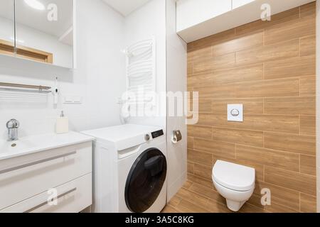 Helles und zeitgenössisches Bad mit Waschmaschine, eleganter Holztäfelung und makellosem weiß, geeignet für moderne Lebensfreude Stockfoto