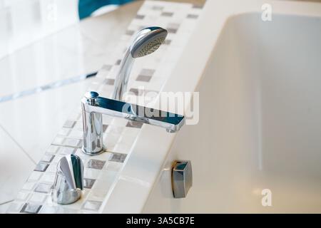 Ein eleganter, glänzender Chrom-Wasserhahn, elegant über einer luxuriösen Badewanne mit modernem Fliesendesign Stockfoto
