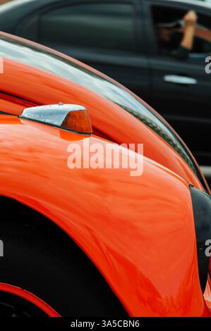 Nahaufnahme des orangefarbenen Oldtimer-Kotflügels mit verschwommenem schwarzem Auto im Hintergrund Stockfoto