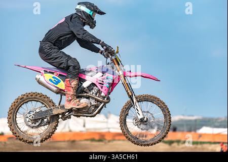 Motocross-Fahrer fliegen während eines Rennens mit Schutzausrüstung auf einem rosa Dirt Bike durch die Luft Stockfoto