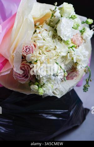 Ein Blumenstrauß in einem Müllbeutel, der verlorene Liebe und verworfene Schönheit symbolisiert. Dieses Bild stellt das Ende einer Beziehung dar, in der die Blumen, einst lebendig und voller Leben, jetzt die emotionale Verschwendung einer gebrochenen Bindung verkörpern. Sie ermutigt zur Reflexion über die flüchtige Natur der Liebe und schärft gleichzeitig das Bewusstsein für Abfall und Umweltfragen. Stockfoto