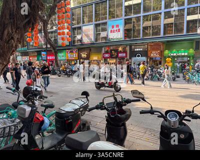Eine geschäftige Straßenszene in Guangzhou, China, voller Motorräder und Fußgänger. Urbanes Leben mit Läden und Laternen. Stockfoto