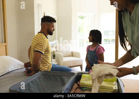 Vater und Tochter reden, während Mutter zu Hause Koffer packt und sich auf die Reise vorbereitet Stockfoto